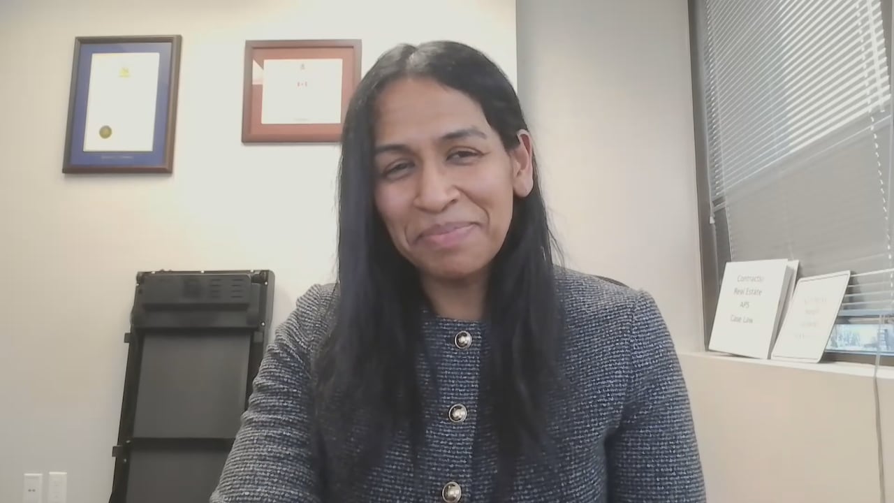 A south Asian woman faces a webcam in an office space.
