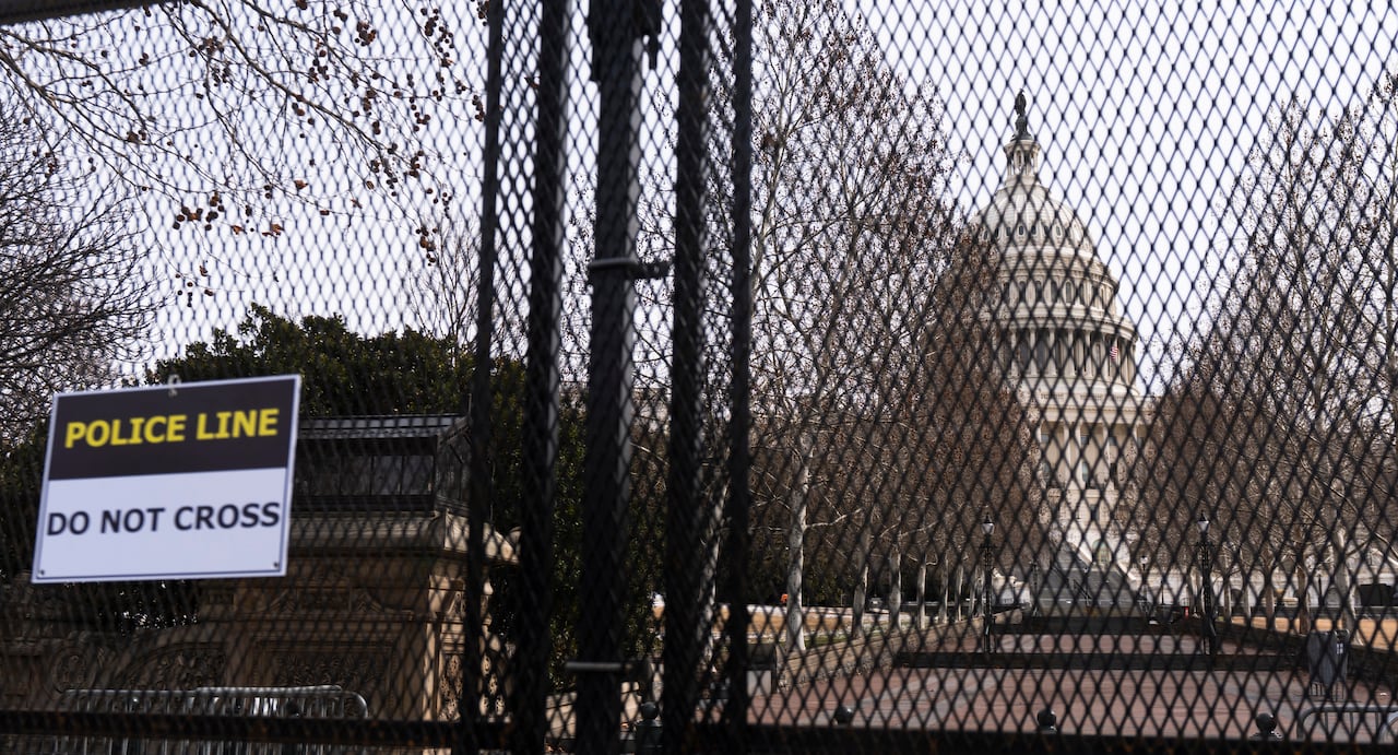 The U.S. Capitol is seen behind the crosshatch of black metal fencing and a sign that reads 'Police Line Do Not Cross'   