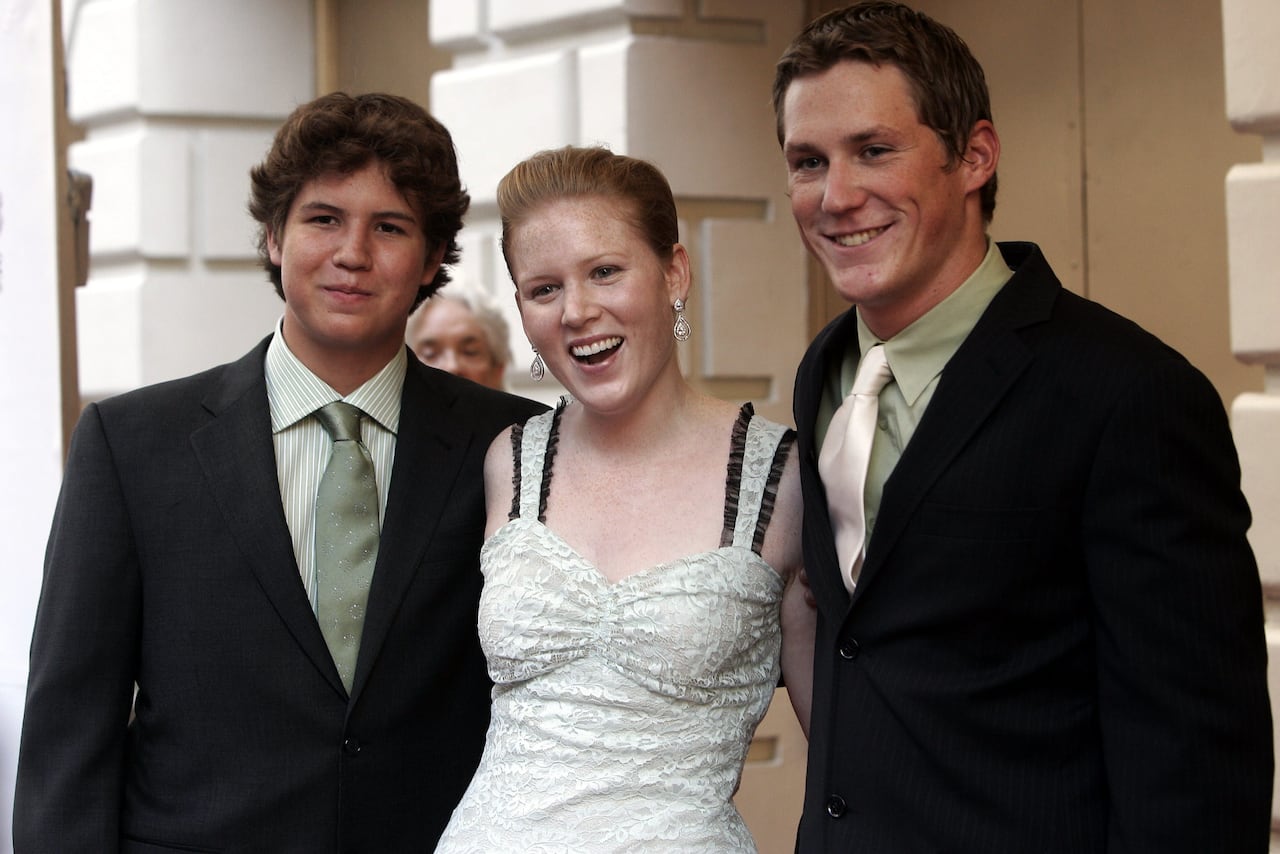Woman in a white dress stands between two young men in suits