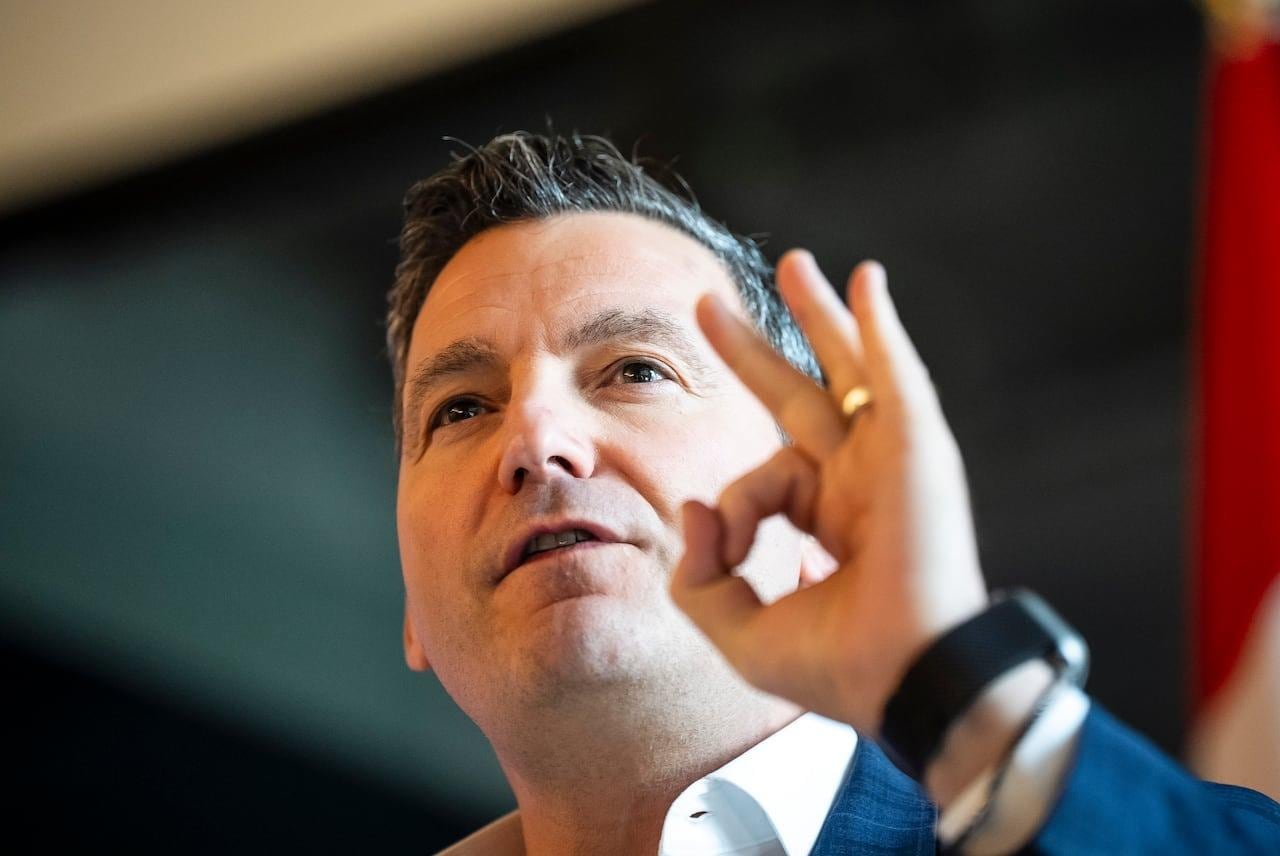 A man in a suit gestures with his hand while speaking at an event.