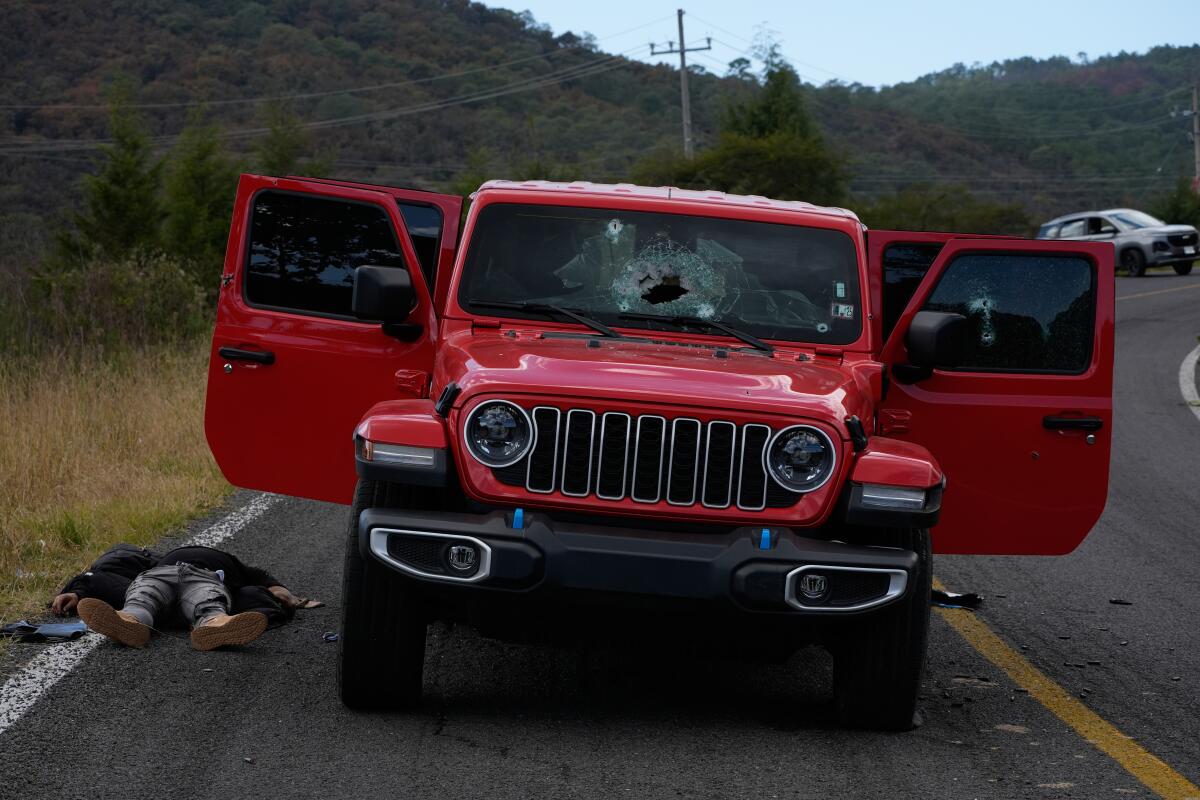 A body lies beside a bullet-riddled red Jeep with a cracked windshield