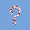 This photo shows many pills, tablets and capsules of varying shapes, colors and sizes arranged in the shape of a question mark on a blue background.