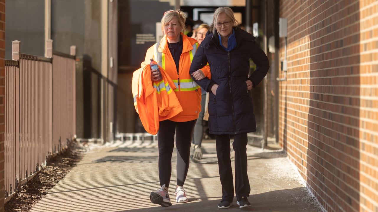 Two women walk out  of a building arm in arm