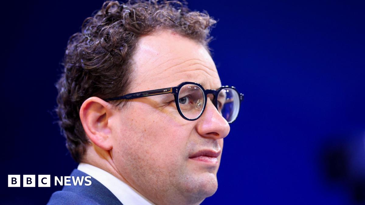 Anthropic CEO Dario Amodei on a stage, furrowing his brow behind round, black-rimmed eye classes.