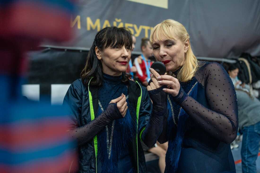 Sunrise cheerleading team members Iryna Nesterenko, 63, sports trainer (left), and Olena Zolotchenko, 57, beauty worker (right), are applying makeup before a performance in Kyiv during Ukraine Cheer Cup competition on Dec. 13, 2025.