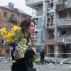 A woman carrying a bouquet of yellow and white flowers walks past a high-rise residential building heavily damaged by a Russian drone strike in the Shevchenkivskyi district of Kyiv, Ukraine, on May 25, 2025.