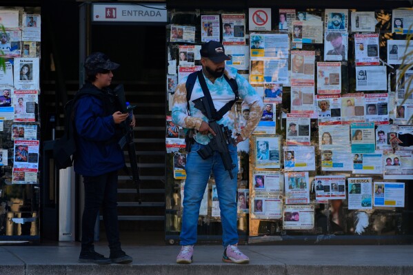 Police officers stand next to posters of missing persons in front of the Special Prosecutor's Office for Missing Persons in Guadalajara, Mexico, Wednesday, Feb. 25, 2026. (AP Photo/Marco Ugarte)