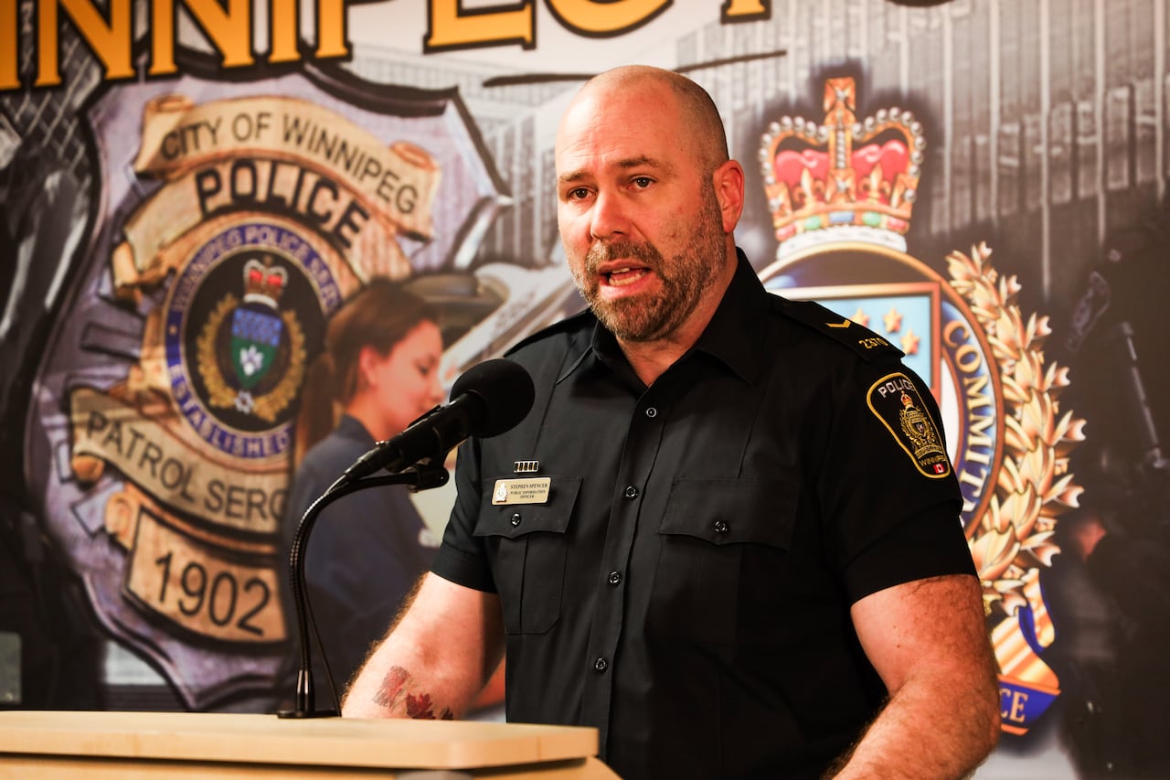 A man in a police uniform stands behind a lectern and speaks into a microphone.