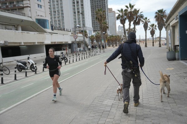 An armed man walks his dogs while a woman jugs after alarms announced that Israel had launched an attack on Iran, in Tel Aviv, Israel ,Saturday, Feb. 28, 2026. (AP Photo/Oded Balilty)