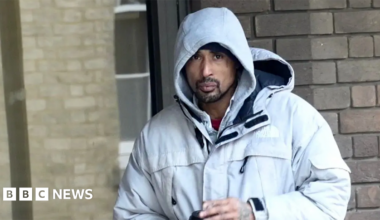 A man wearing a grey hoodie and a grey jacket. He is holding a coffee cup.