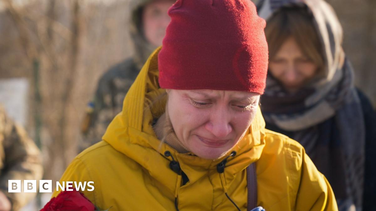 Roman, a Ukrainian soldier in a drone repair unit, holds up an unmanned aerial vehicle and faces the camera. He's in his green army uniform.