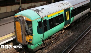 An elevated side view of a green and yellow Govia Thameslink train sitting at a platform.
