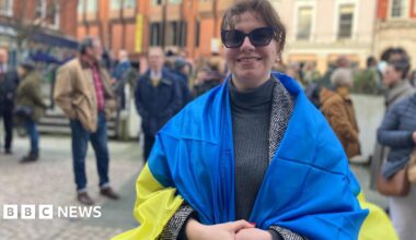 Nataliia Revkova and Nadiia Hoian smile at the camera. They are sat next to each other in a radio studio. Nataliia has dark hair that is tied up and she has a fringe. Headphones rest around her neck. Nadiia has long blonde hair that is tied up and she wears her headphones.