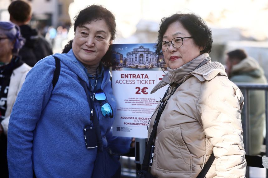 Tourists pose next to a sign indicating the newly introduced two‑euro entry fee.