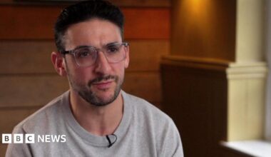 Yoni Finlay stares forward while wearing a grey sweatshirt. He has black hair and is wearing transparent glasses.