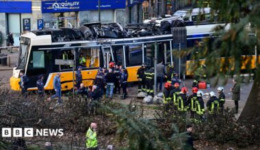 Emergency workers stand near damaged tram at scene of crash