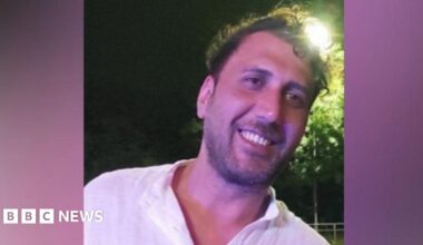 Mustafa Qays Obadey smiles while wearing a white shirt. He is posing at night with a street light seen shining behind his head.