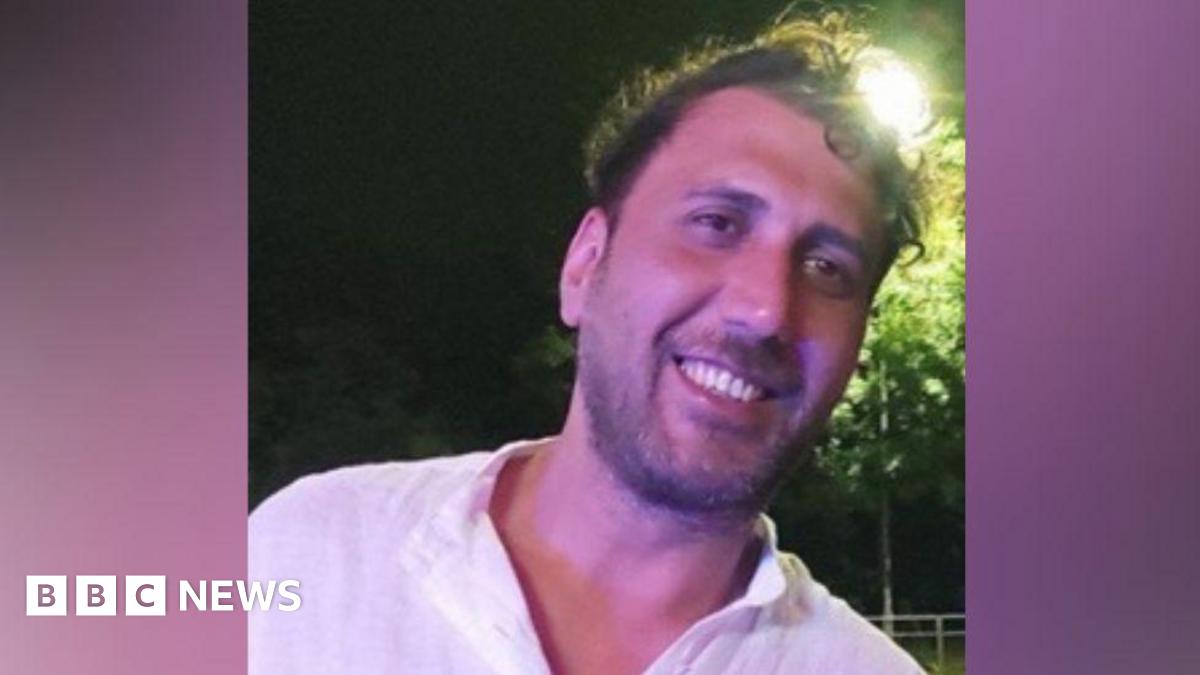Mustafa Qays Obadey smiles while wearing a white shirt. He is posing at night with a street light seen shining behind his head.