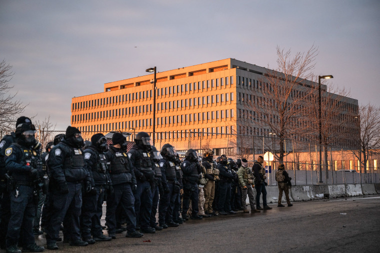 Federal law enforcement officers watch as demonstrators against the Immigration and Customs Enforcement (ICE) deployment protest outside the Bishop Henry Whipple Federal Building in St. Paul, MN.