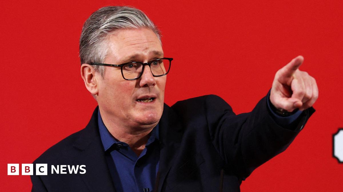 Keir Starmer in a blue shirt and black blazer standing in front of a red background pointing into the distance.