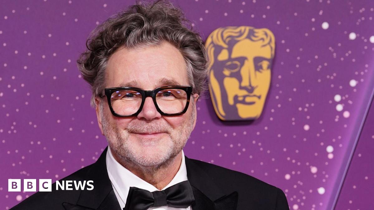 Kirk Jones in a tuxedo at the Baftas, he has glasses and grey, wavy hair