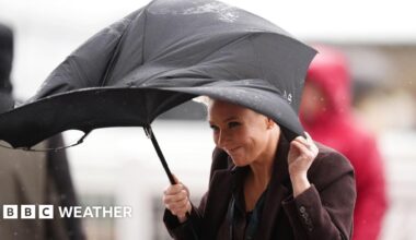 A woman struggles to straighten her windswept umbrella as she stands in the rain.