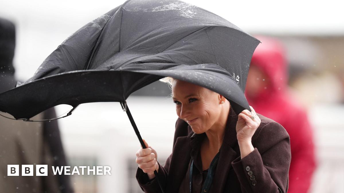 A woman struggles to straighten her windswept umbrella as she stands in the rain.