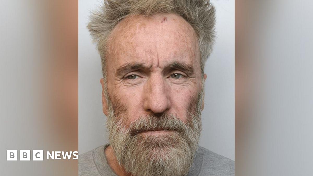 Police custody image of Tony Devenport with dishevelled grey hair and beard wearing a grey top.