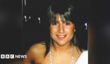 Jenna Watkins is a white woman in her early 20s in a head and shoulders photo. She has dyed black hair which is shoulder length with a fringe. She is wearing an off the shoulder white top and a long silver necklace with large beads starting at her collarbone. She is wearing make up and looks like she is on a night out. She is smiling straight at the camera. The background is black.