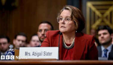 A woman wearing a red suit sits in front of a microphone.