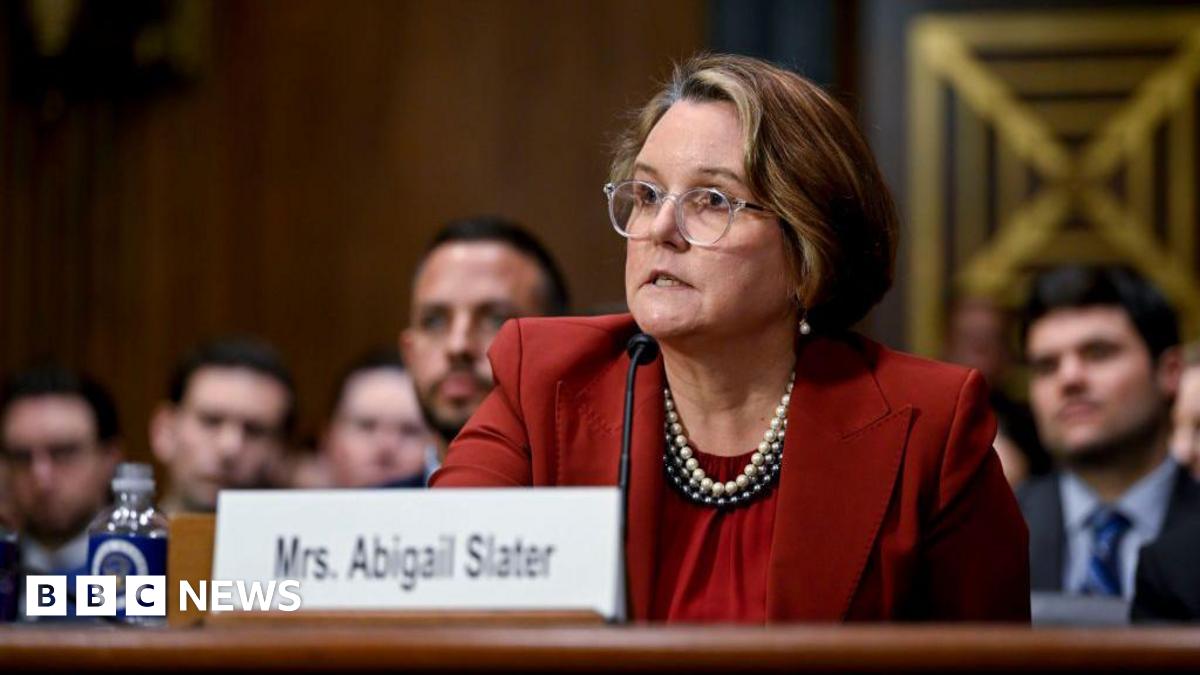 A woman wearing a red suit sits in front of a microphone.