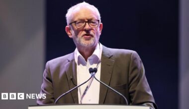 Jeremy Corbyn, who is dressed in a grey suit jacket and white shirt, speaks at a podium with two microphones.