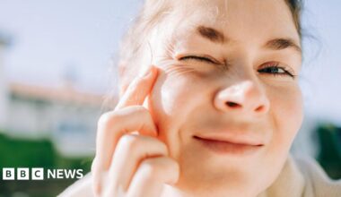 A woman, standing in the sunshine, examining her eye wrinkles