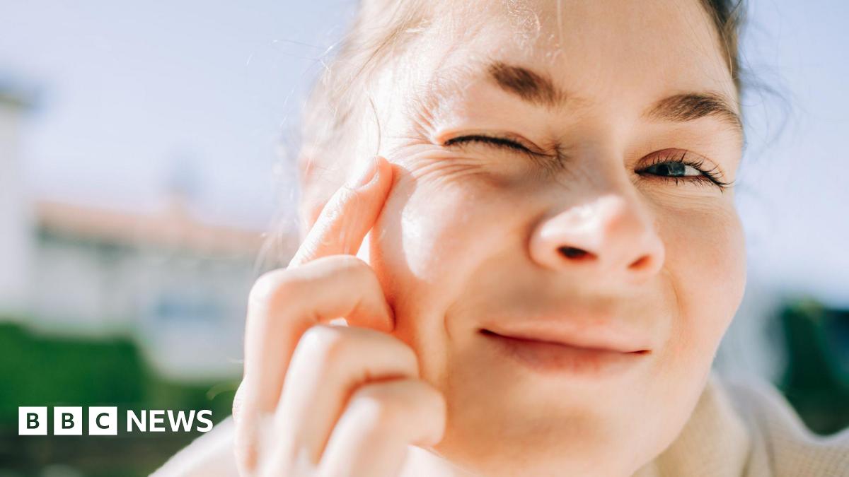 A woman, standing in the sunshine, examining her eye wrinkles