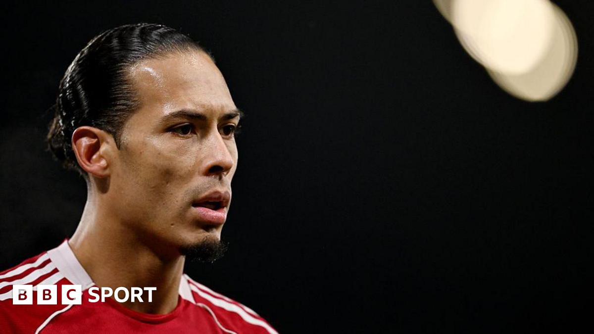 Close-up image of Virgil van Dijk in the left of the photograph. He has black hair, tied back, and is wearing Liverpool's red home shirt. The background of the image is black with a spotlight in the top right corner.