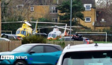 Two helicopters on the ground in an urban park.