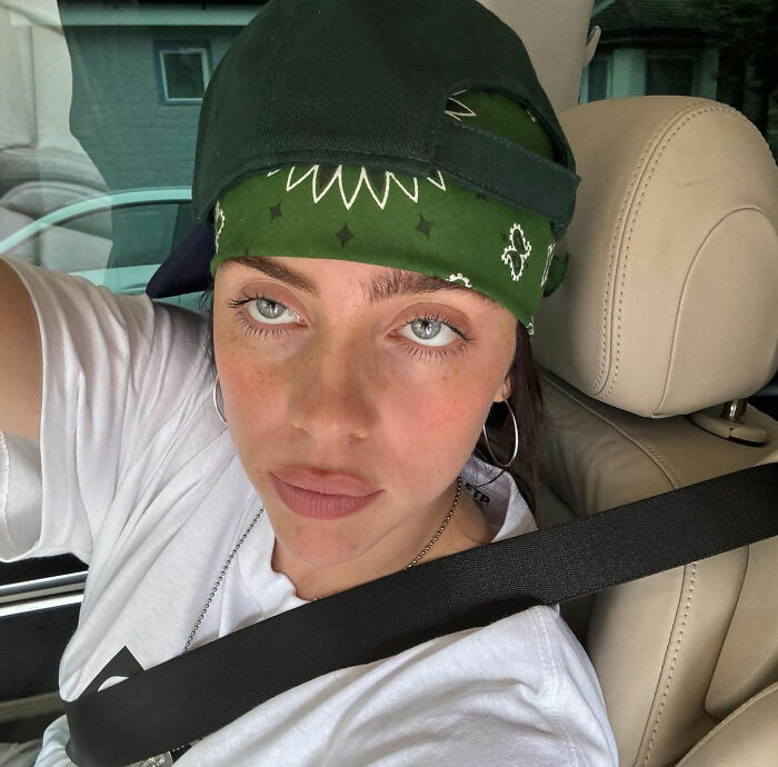 Billie Eilish wearing a green bandana and cap, taking a selfie in a car, amid Grammys rant and lavish lifestyle criticism.
