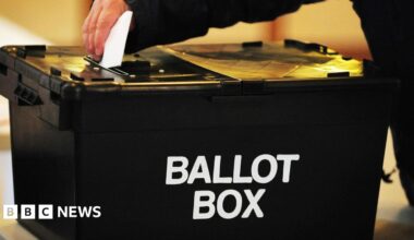 A voter placing a ballot paper in a black ballot box at a polling station.