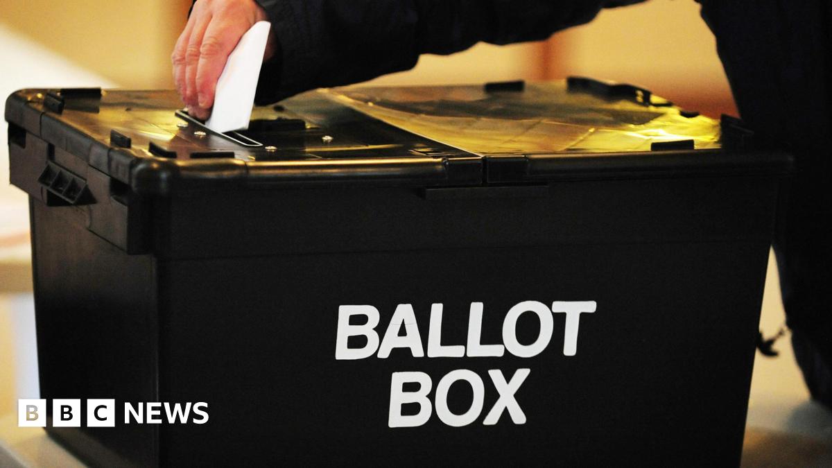 A voter placing a ballot paper in a black ballot box at a polling station.