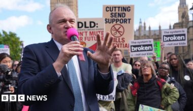 A fossil of part of a crinoid that resembles a row of teeth. The markings form a curved shape with pale, tooth‑like segments set against the darker surface of the fossil. The fossil rests on another rock in the foreground.