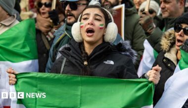 A crowd of of people pictured waving flags and making peace signs with their hands