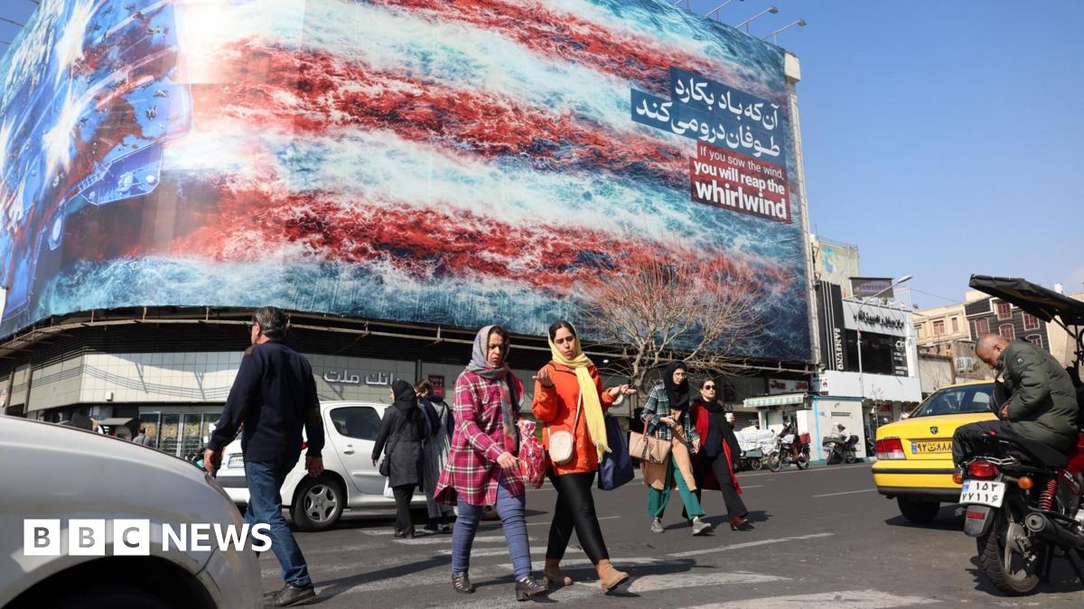 Iranians walk past a billboard warning the US not to attack Iran at a square in central Tehran, Iran (25 February 2026)