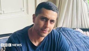 A woman with shoulder length light hair wearing black rimmed glasses looking at the camera