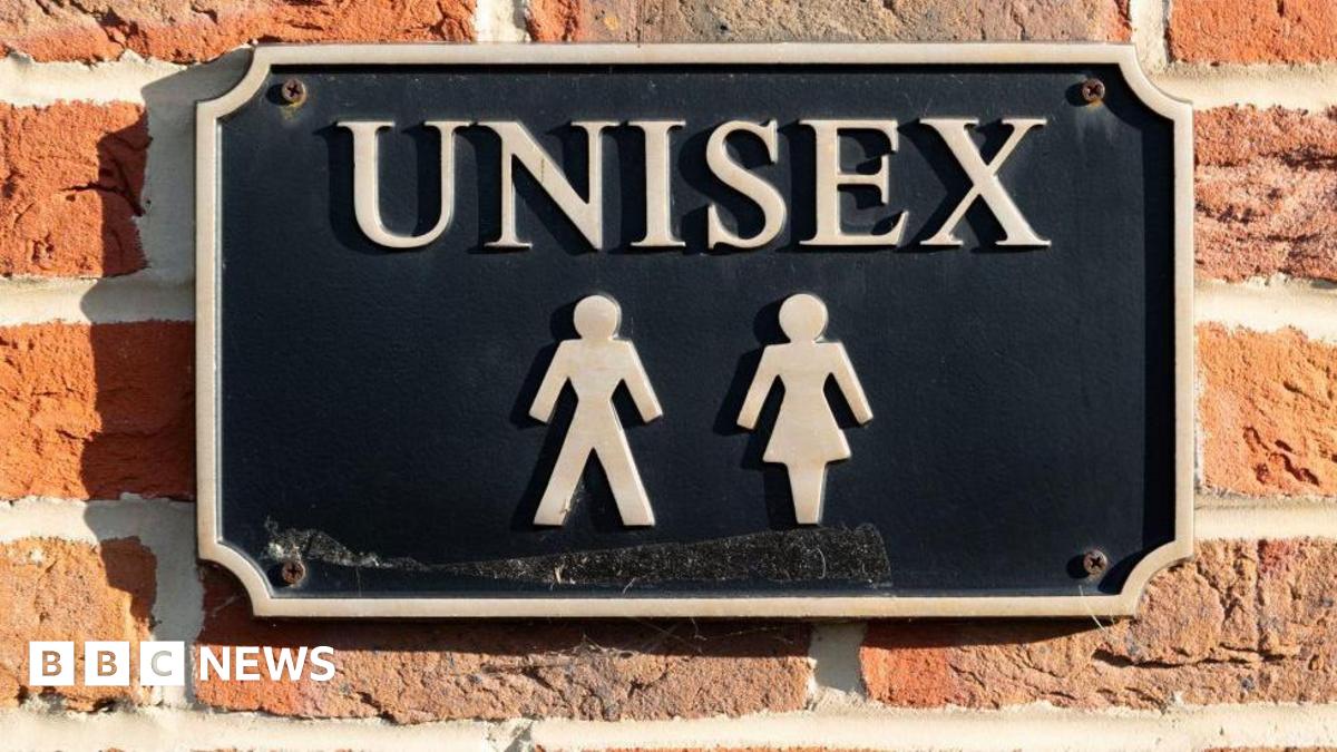 A sign that reads "unisex" on a brick wall in an unknown location.