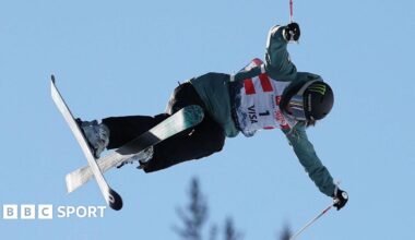 Freestyle skier Zoe Atkin is airborne, with only a blue sky and the tops of trees visible behind her
