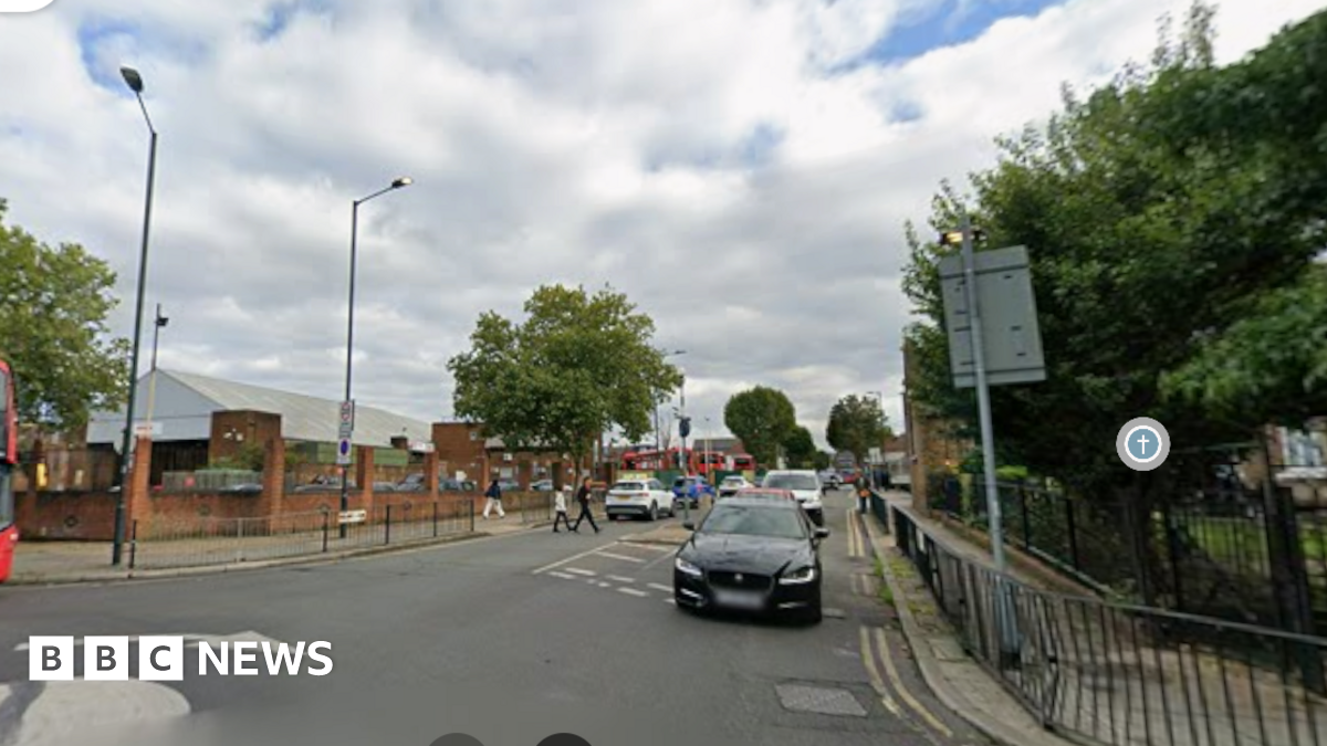 Google street view image of Pound Lane from its junction with High Road, showing a road with several cars, pedestrians and what looks like a large grocery store to the left.