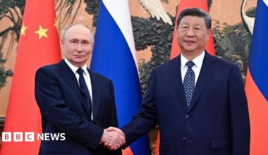 Vladimir Putin and Xi Jinping shake hands, with the flags of Russia and China in the background