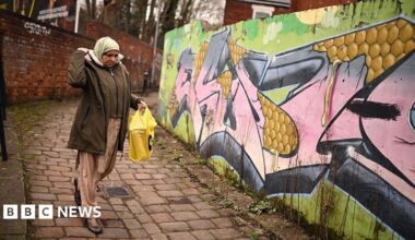 A woman passes graffiti sprayed on the wall of an alleyway in Longsight, within the Gorton and Denton parliamentary constituency