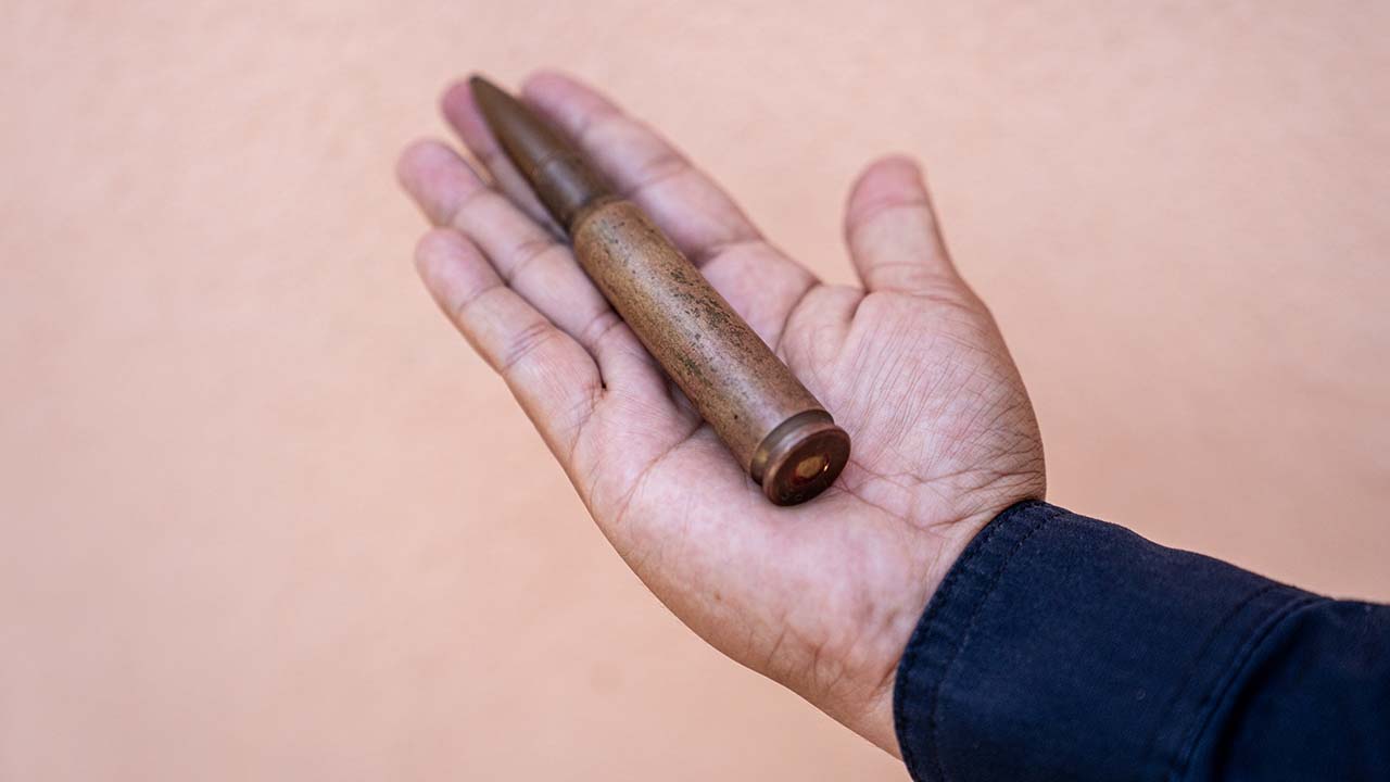 Photo of a hand holding a .50 caliber round of ammunition, which takes up most of the outstretched hand.