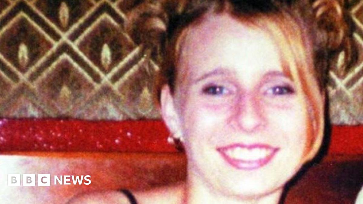 A grainy image of Victoria Hall smiling at the camera, with her blonde hair swept down to one side. She is wearing bright lipstick and an earring.